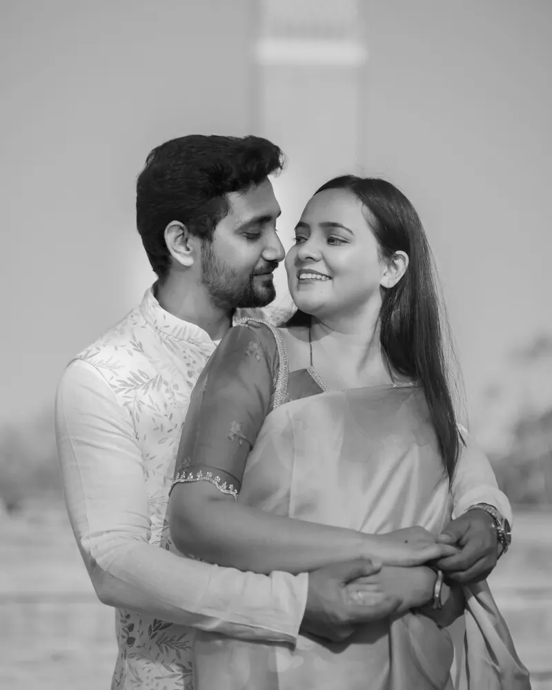 Black and white portrait of a couple embracing cheek to cheek, both smiling, her hands over his at the waist.