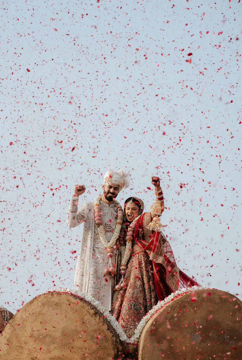 Bride and groom raise their arms in celebration under a shower of rose petals, two drums in the foreground.