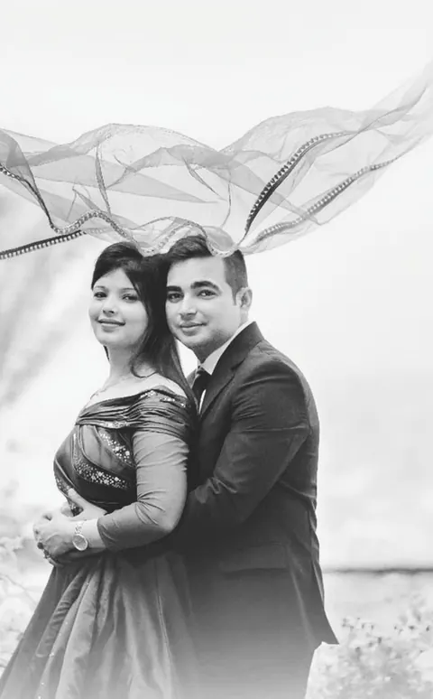 Ashish and Megha. Black and white portrait of the couple standing close, a sheer dupatta lifting in the wind above them.